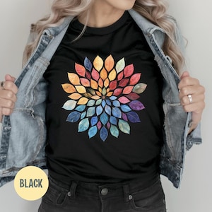 K&ouml;nnte beinhalten: Ein schwarzes T-Shirt mit einer kreisf&ouml;rmigen Mandala-Grafik, die aus zahlreichen kleinen, mehrfarbigen Bl&auml;ttern in einem radialen Muster besteht. Die Bl&auml;tter zeigen einen Farbverlauf von warmen Gelb-, Orange- und Rott&ouml;nen bis hin zu k&uuml;hlen Blau- und Violettt&ouml;nen.