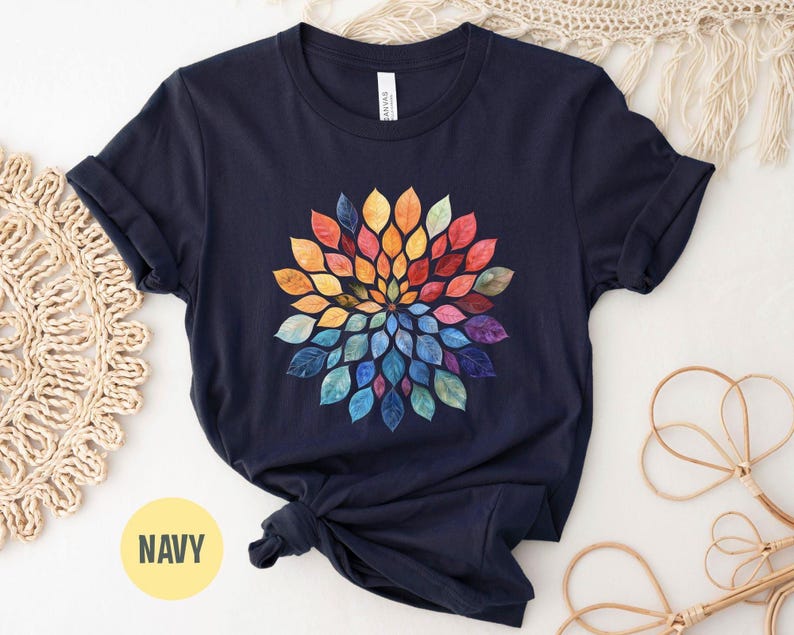 K&ouml;nnte beinhalten: Ein marineblaues Kurzarm-T-Shirt mit einer kreisf&ouml;rmigen Mandala-Grafik, die aus aquarellartigen Bl&auml;ttern in einem Farbspektrum aus Gelb, Orange, Rot, Violett und Blau besteht und in einem radialen Muster auf der Brust angeordnet ist.
