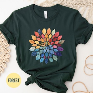 K&ouml;nnte beinhalten: Ein dunkelwaldgr&uuml;nes Kurzarm-T-Shirt mit einer kreisf&ouml;rmigen Mandala-Grafik, die aus mehrfarbigen Bl&auml;ttern im Aquarellstil besteht, welche strahlenf&ouml;rmig angeordnet sind und von warmen Gelb- und Oranget&ouml;nen zu k&uuml;hlen Blau- und Violettt&ouml;nen &uuml;bergehen.