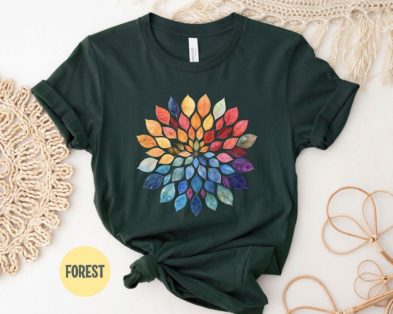 K&ouml;nnte beinhalten: Ein dunkelwaldgr&uuml;nes Kurzarm-T-Shirt mit einer kreisf&ouml;rmigen Mandala-Grafik, die aus mehrfarbigen Bl&auml;ttern im Aquarellstil besteht, welche strahlenf&ouml;rmig angeordnet sind und von warmen Gelb- und Oranget&ouml;nen zu k&uuml;hlen Blau- und Violettt&ouml;nen &uuml;bergehen.