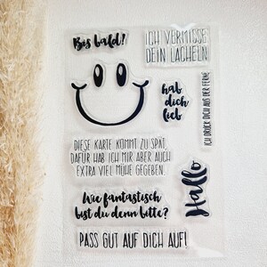 Könnte beinhalten: Klare Acrylstempel mit schwarzem Text und einem Smiley-Gesicht. Sätze sind "Bis bald!", "Ich vermisse dein Lächeln", "Hallo" und "Pass gut auf dich auf!". Ideal für Scrapbooking und Kartenherstellung.