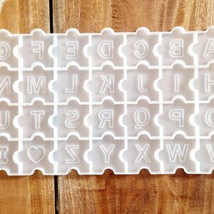 Könnte beinhalten: Weiße Silikonform mit einem Puzzle-ähnlichen Design mit den Buchstaben des Alphabets, einem Herzen und einem Knochen.