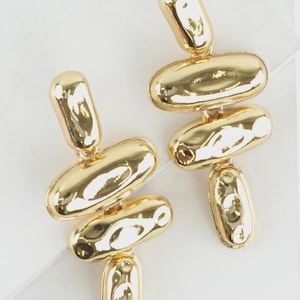 May include: A pair of gold-toned drop earrings featuring a series of interconnected, smooth, and reflective oval-shaped metal links. The design consists of four distinct, rounded segments arranged in a vertical, slightly staggered formation.