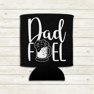 Op de afbeelding: Zwarte koelbox voor blikjes met witte tekst "Dad Fuel" en een afbeelding van een bierglas met schuim.