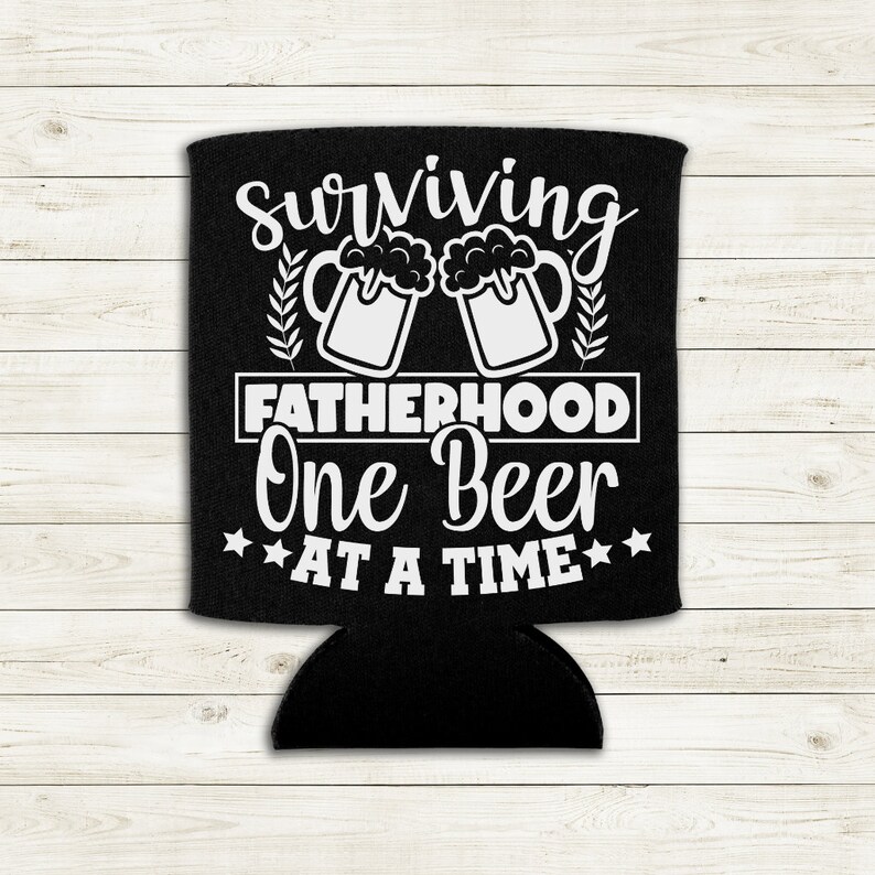 Op de afbeelding: Zwarte neopreen-blikjeskoeler met witte tekst die "Surviving Fatherhood One Beer At A Time" luidt. Het ontwerp bevat twee witte bierglazen met schuim erop.