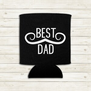 Op de afbeelding: Zwarte blikjeskoeler met een witte snor en de tekst "BEST DAD" erop gedrukt.