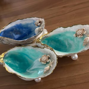 May include: Three white seashell dishes with gold trim, each filled with blue or green resin and decorated with small white turtle figurines.