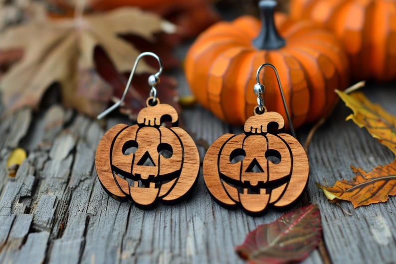Peut inclure: Boucles d'oreilles en bois en forme de citrouille avec crochets argent&eacute;s. Chaque boucle d'oreille est sculpt&eacute;e en forme de lanterne d'Halloween souriante. Les boucles d'oreilles sont pr&eacute;sent&eacute;es sur une surface en bois avec des citrouilles et des feuilles d'automne.