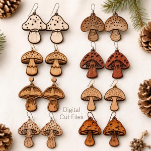 May include: A collection of wooden mushroom earrings in various designs. Some earrings feature dotted caps, while others have intricate cut-out patterns. The earrings are displayed on a white surface with pine cones and greenery. The text "Digital Cut Files" is visible.