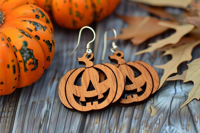 Peut inclure: Boucles d'oreilles en bois en forme de citrouilles souriantes avec des crochets en argent. L'arri&egrave;re-plan pr&eacute;sente des citrouilles oranges et des feuilles d'automne, parfaites pour Halloween.