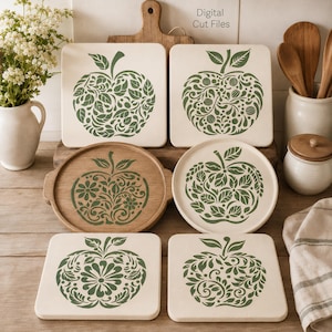 May include: A selection of kitchenware with a green apple motif. The items include square and round coasters, a wooden tray, and a cutting board. The apple design is filled with intricate floral and leaf patterns. The text "Digital Cut Files" is visible.