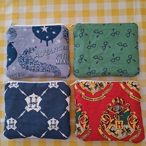 May include: Four square, zippered pouches with different patterns. One is light blue with stars and the text "ADVANCED POTION MAKING". Another is green with glasses. The third is navy blue with "H" and lightning bolts. The last is red with a crest.