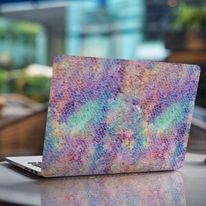 May include: A laptop computer with a colorful iridescent mermaid scale pattern on the lid. The laptop is closed and sitting on a table.