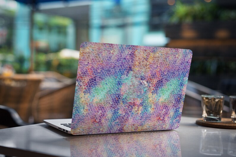 May include: A laptop computer with a colorful iridescent mermaid scale pattern on the lid. The laptop is closed and sitting on a table.