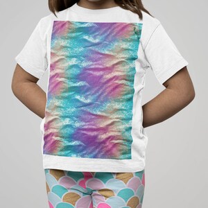 May include: A white t-shirt with a colorful tie-dye design. The shirt is being worn by a child with pink and blue leggings that have a mermaid scale pattern.