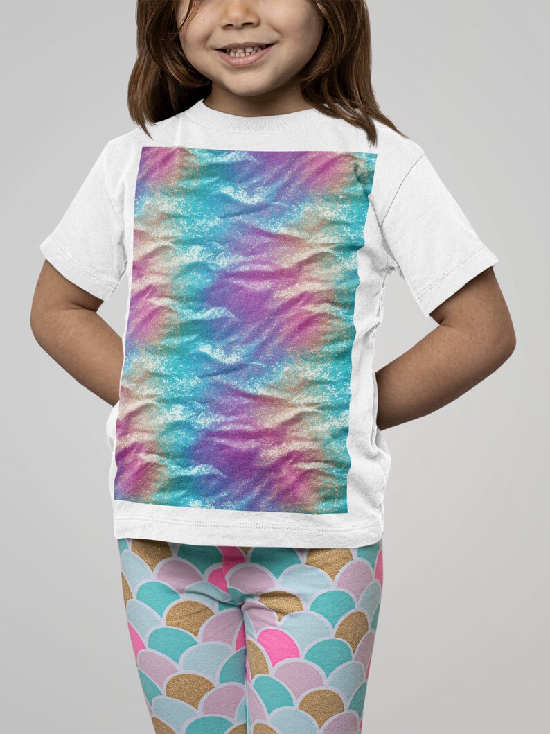 May include: A white t-shirt with a colorful tie-dye design. The shirt is being worn by a child with pink and blue leggings that have a mermaid scale pattern.