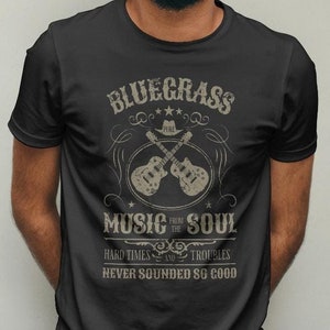 May include: A black t-shirt with a vintage-style graphic design featuring the text "Bluegrass Music from the Soul", two crossed guitars, and the phrase "Hard Times and Troubles Never Sounded So Good".