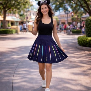 May include: A navy blue skater skirt with a pattern of colourful lightsabers and stars. The skirt has a high waist and a flared silhouette. The lightsabers are in red, blue, green, and yellow. The skirt is worn with a black vest top and white trainers.