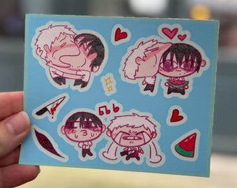 May include: A light blue sticker sheet featuring cartoon illustrations of two characters in various poses. The illustrations include images of characters embracing, a knife, a watermelon slice, and musical notes. Red hearts are scattered throughout the design.