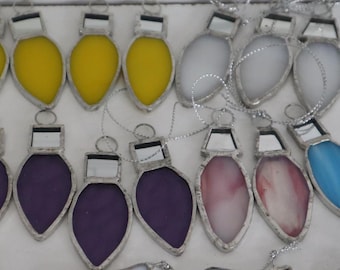 May include: A collection of stained glass ornaments shaped like light bulbs, each featuring a metallic solder frame and a silver hanging loop. The ornaments come in various colors including yellow, white, red, purple, pink, and blue glass.