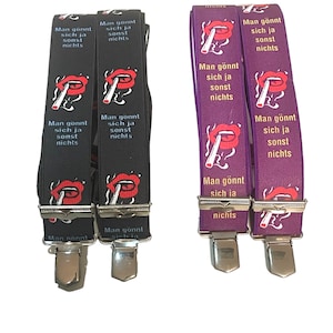 Könnte beinhalten: Ein Paar schwarze und violette Hosenträger mit einem roten Lippen- und Zigarettenmotiv. Die Hosenträger haben den Text "Man gönnt sich ja sonst nichts" aufgedruckt.