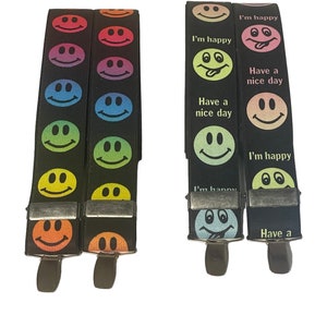 Op de afbeelding: Zwarte bretels met regenboogkleurige smiley gezichten. Eén paar heeft de tekst "I'm happy" en "Have a nice day". De bretels hebben metalen clips en zijn een leuk accessoire.