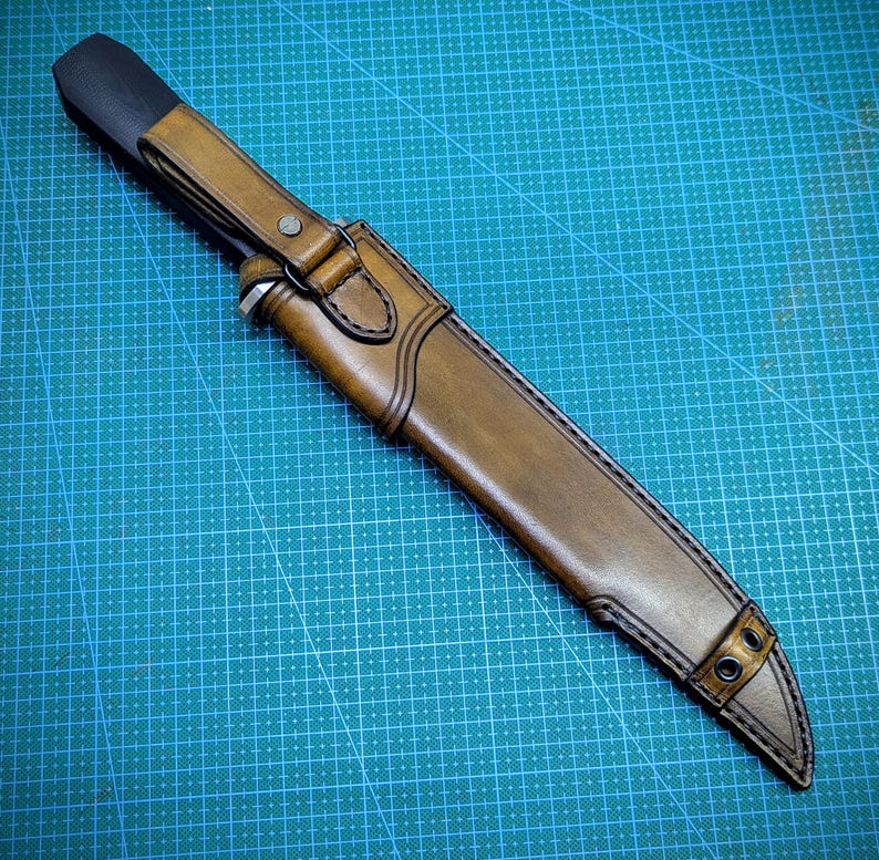 May include: A handcrafted leather knife sheath in shades of brown, with a black handle cover. The sheath features detailed stitching and metal rivets, designed to securely hold a knife. The design suggests a focus on durability and craftsmanship.