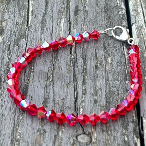 Op de afbeelding: Een rode kristallen armband met een zilveren sluiting. De armband is gemaakt van kleine, gefacetteerde kristallen die in het licht glinsteren.