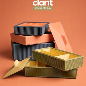 Könnte beinhalten: Ein Set stapelbarer Boxen mit der Aufschrift clarit stackable box, bestehend aus rechteckigen Behältern mit gerippten Außenwänden in Dunkelgrau, Orange und Olivgrün, inklusive passender Deckel und kontrastierender Inneneinteilungen.