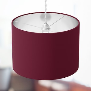 May include: A burgundy fabric lampshade with a white cord and a silver ceiling fixture.