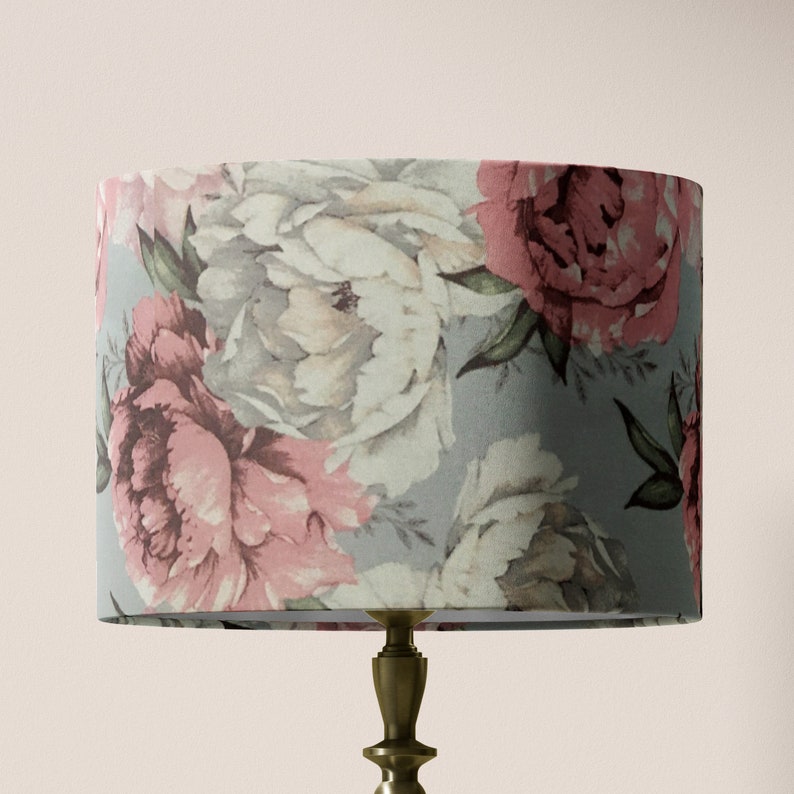 K&ouml;nnte beinhalten: Ein grauer Lampenschirm mit einem floralen Muster aus rosa und wei&szlig;en Pfingstrosen. Der Lampenschirm ist zylindrisch und hat eine wei&szlig;e Innenauskleidung.