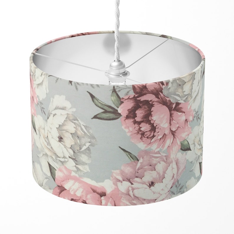 K&ouml;nnte beinhalten: Ein wei&szlig;er Lampenschirm mit einem floralen Muster mit rosa und wei&szlig;en Pfingstrosen auf hellblauem Hintergrund.