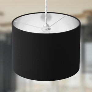 Op de afbeelding: Zwarte lampenkap van stof met een witte binnenkant. De lampenkap is cilindrisch en heeft een eenvoudig ontwerp.