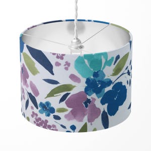 Può includere: Un paralume bianco con un motivo floreale in tonalità di blu, verde e viola. I fiori sono dipinti in stile acquerello.