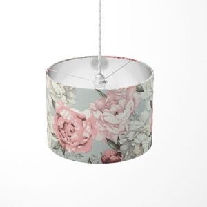 K&ouml;nnte beinhalten: Ein wei&szlig;es Kabel h&auml;ngt von einer Decke mit einer daran befestigten Leuchte. Die Leuchte hat einen runden, wei&szlig;en Stoffschirm mit einem floralen Muster aus rosa und wei&szlig;en Pfingstrosen auf hellblauem Hintergrund.