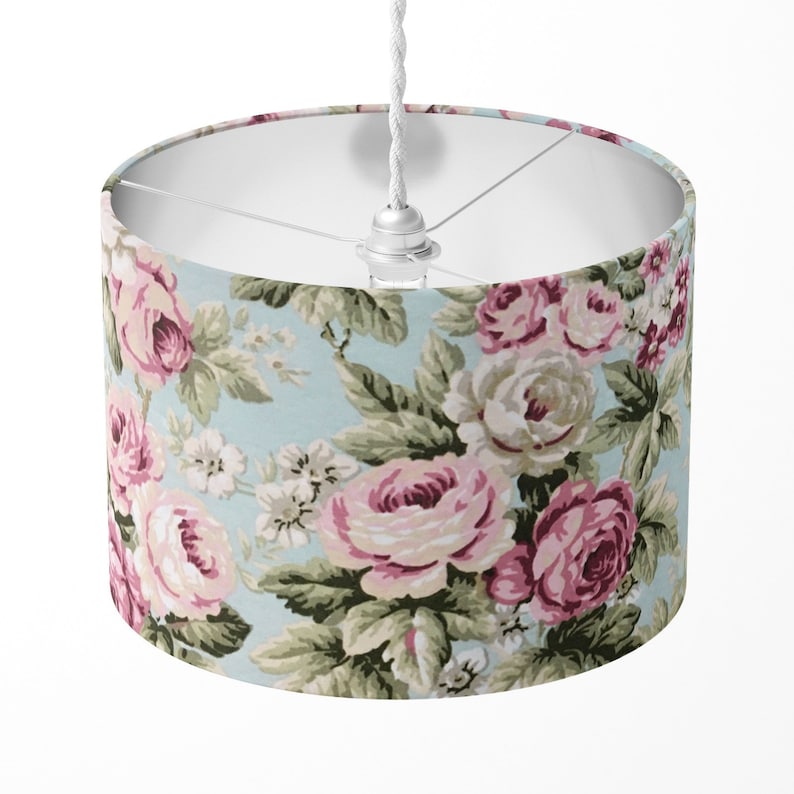 Peut inclure: Un abat-jour en tissu blanc avec un motif floral compos&eacute; de roses roses et blanches sur fond bleu clair.