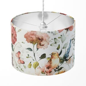 May include: A white drum lampshade with a floral pattern featuring pink and orange flowers, green leaves, and a yellow bird. The pattern is reminiscent of watercolour painting.