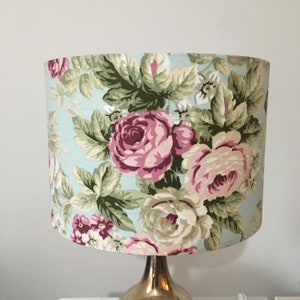 Peut inclure: Un abat-jour de lampe bleu clair avec un motif floral compos&eacute; de roses roses et blanches et de feuilles vertes.