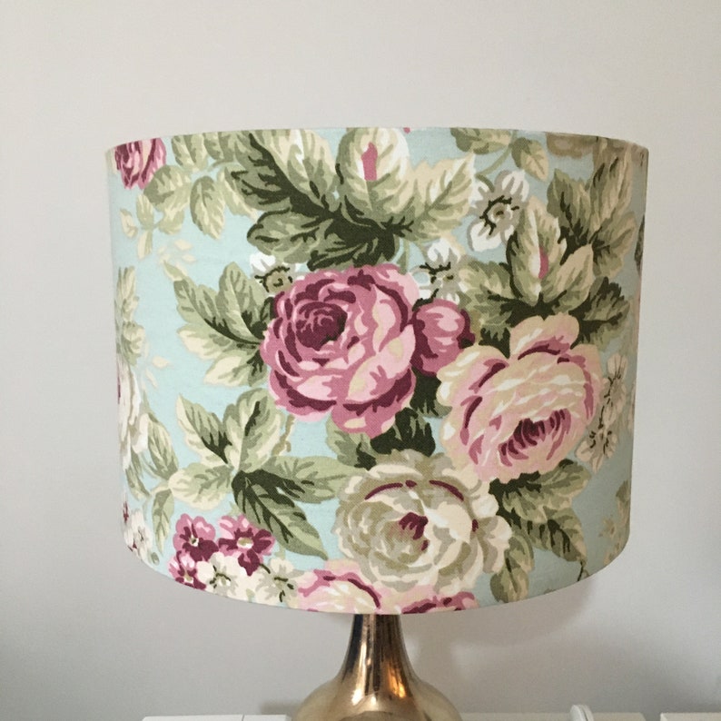 Peut inclure: Un abat-jour de lampe bleu clair avec un motif floral compos&eacute; de roses roses et blanches et de feuilles vertes.