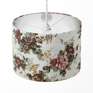 Peut inclure: Un abat-jour blanc avec un motif floral composé de roses roses et rouges, de feuilles vertes et de fleurs jaunes sur un fond crème.