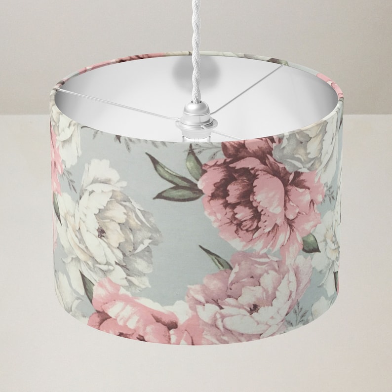K&ouml;nnte beinhalten: Ein wei&szlig;er Lampenschirm mit einem floralen Muster mit rosa und wei&szlig;en Pfingstrosen auf hellblauem Hintergrund.