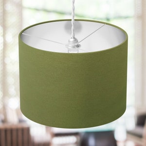 May include: A green fabric lampshade with a white interior. The lampshade is cylindrical and has a simple design.