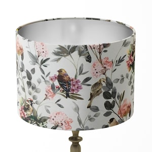 May include: A white lampshade with a floral pattern featuring birds and pink flowers. The lampshade has a silver lining.