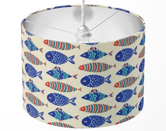 May include: A white drum lampshade with a pattern of blue and red fish on a cream background.
