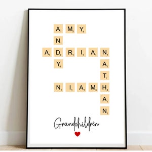 Puede incluir: Un fondo blanco con los nombres Amy, Adrian, Niamh y Ath impresos en letras negras sobre fichas de Scrabble beige. El texto "Grandchildren" está escrito en cursiva negra con un corazón rojo debajo.