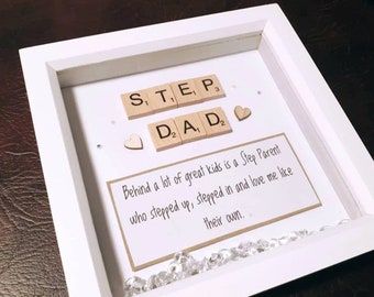 Può includere: Cornice per foto bianca con sfondo beige. La cornice contiene le parole "STEP DAD" scritte con tessere di lettere in legno. Lo sfondo include anche il testo "Behind a lot of great kids is a Step Parent who stepped up, stepped in and love me like their own."