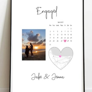Pode incluir: Uma impressão emoldurada branca com a palavra "Engaged" escrita em itálico preto. A impressão apresenta uma foto de um casal em uma praia ao pôr do sol, um calendário com um coração marcando a data de seu noivado e um mapa em forma de coração com um coração rosa marcando uma localização. O texto "Jake & Jenna" está escrito em itálico preto na parte inferior da impressão.