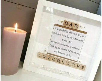 Può includere: Una cornice bianca con un messaggio scritto su un pezzo di carta all'interno. Il messaggio dice "Se cercassimo in tutto il mondo, non troveremmo mai un papà che sia più premuroso o più gentile. Speriamo che tu appenda questo e lo guardi ogni giorno e ricordi che ti amiamo più di quanto le parole possano dire." Il messaggio è circondato da piccoli cuori bianchi e le parole "PAPÀ" e "TANTO AMORE" sono scritte con tessere di lettere.