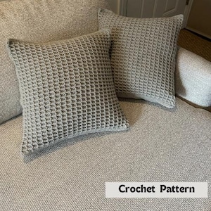 May include: Two grey crocheted throw pillows with a waffle stitch pattern. The pillows are on a grey sofa. Crochet Pattern.
