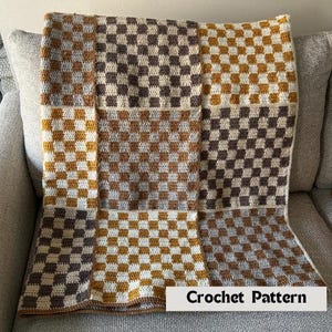 Könnte beinhalten: Handgefertigte Häkeldecke mit Schachbrettmuster in Braun-, Beige- und Goldtönen. Die Decke liegt auf einem grauen Sofa. Der Text "Crochet Pattern" ist unten zu sehen.